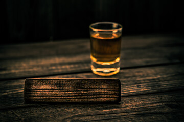 Glass of tequila with the empty wooden plank on an old wooden table. Angle view, focus on the wooden plank