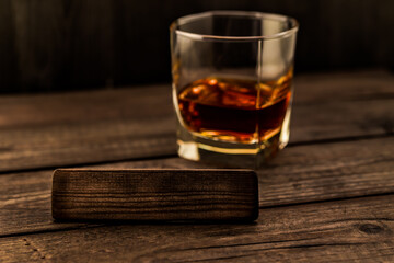 Glass of brandy with the empty wooden plank on an old wooden table. Angle view, focus on the wooden plank