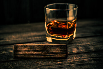 Glass of brandy with the empty wooden plank on an old wooden table. Angle view, focus on the wooden plank