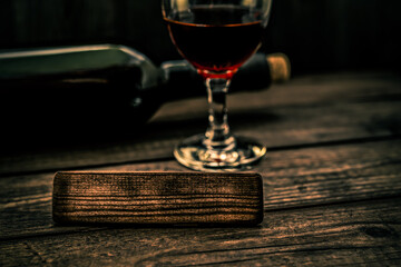 Glass and bottle of red wine with the empty wooden plank on an old wooden table. Angle view, focus on the wooden plank