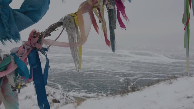Colored khadak ribbons on the tree of desires and a group of people descending the hill to the ice-covered Lake Baikal
