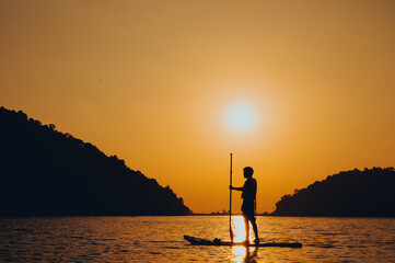 Paddle standing, silhouette of man on the beach at sunset