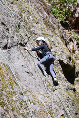 A young girl is climbing a rock. A girl with a rope engaged in the sports of rock climbing on the rock.	
