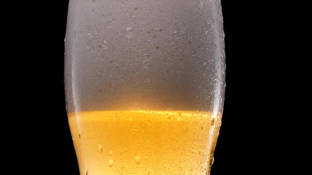 Cold light beer in a glass with water drops. Beer mug close up on a black background. Beer foam.