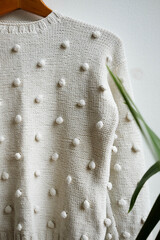 White knitted sweater hanging on monstera background