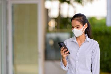 Happy woman wearing face mask to protect from coronavirus Covid-19 while using phone