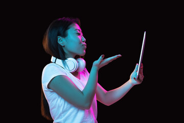 Obraz premium Asian young woman's portrait on dark studio background in neon. Concept of human emotions, facial expression, youth, sales, ad.