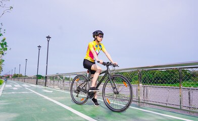 Young Asian healthy cyclist girl wearing helmet cycling and yellow shirt riding bike on bicycle...