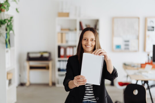 Happy smiling businesswoman holding up a blank white notebook