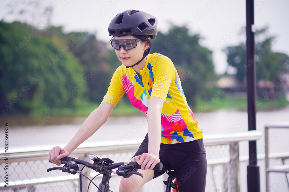 Wall mural portrait image of young asian cyclist girl wearing helmet cycling and yellow shirt riding bike, heal