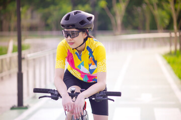 Portrait image of Young Asian cyclist girl wearing helmet cycling and yellow shirt riding bike, healthy lifestyle concept.