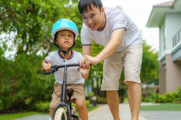 Asian father  teaching his child how to ride a bicycle in a neighborhood garden, fathers interact...