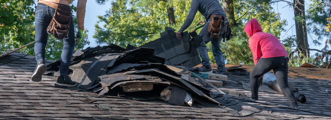 Roofers removing old material from a house in preparation for storm damage repair.