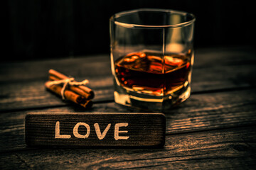 Glass of brandy with cinnamon sticks tied with jute rope and the wooden plank on it is an inscription 