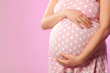 Close-up of unrecognizable pregnant woman with hands over tummy at pink background