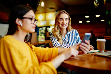 Smiling women watching video on smartphone in cafe