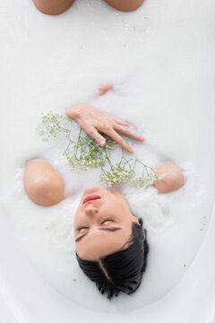 overhead view of sensual woman with white, tiny flowers relaxing in milk bath.