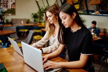 Wistful women working on laptops in cafe