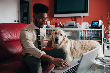 Young black man lying couch with dog using computer