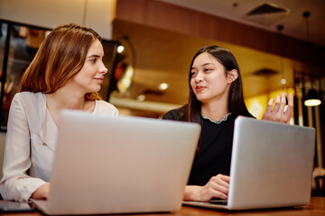 Diverse cheerful women discussing job while working with laptops