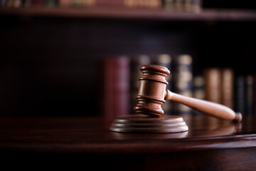 Lawyer office. Gavel on brown shining desk and collection of legal books in the bookshelf.