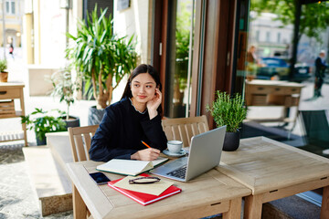 Young ethnic student preparing for exam sitting with laptop in cafeteria