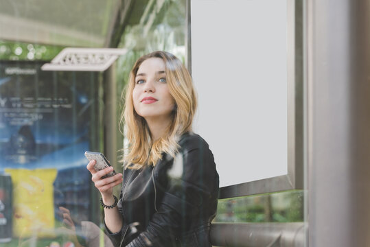 Young Woman Commuter Sitting At Bus Stop Waiting