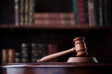 Lawyer office. Gavel on brown shining desk and collection of legal books in the bookshelf.