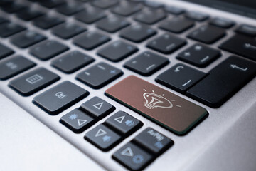 Laptop keyboard with a orange key with an idea symbol represented by a lit light bulb. Concept of idea, eureka, invention, online