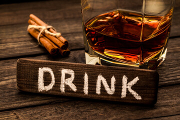 Glass of brandy with cinnamon sticks tied with jute rope and the wooden plank on it is an...