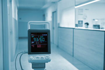 Hospital equipment to measure blood pressure in a hospital corridor with an out-of-focus nurse sitting at the back.