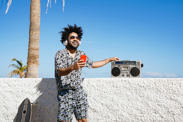Fototapeta premium Trendy mulitracial man with vintage boombox and smartphone in the city - Young skater guy outdoor