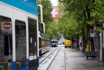 Tram at famous Bahnhofstrasse at Zurich City at rainy spring day with green trees and Swiss flag...