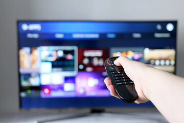 Smart TV remote controller in female hand on screen background. Woman choosing streaming services,...