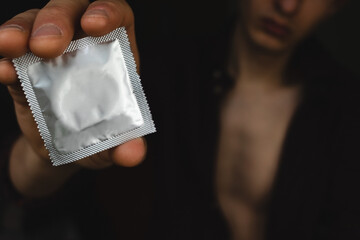 Guy gives a condom in close-up on a dark background