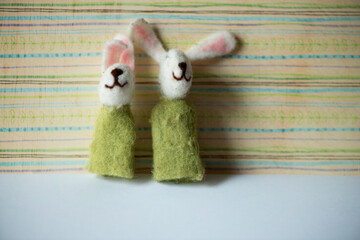 two white rabbit in a green cloak finger puppets posing against a striped green and blue background