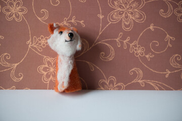 a red fox finger puppet posing against a brown floral background
