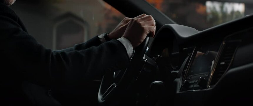 CU on hands of 40s Caucasian business man wearing a suit driving his luxury car through wealthy neighborhood. Shot with 2x anamorphic lens