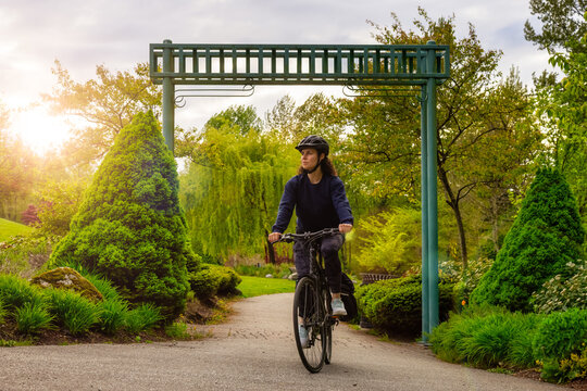 Adult Caucasian Woman Riding a Bicycle on a path in a modern city park. Spring Evening. Taken in Hawthorne Rotary Park, Surrey, Vancouver, British Columbia, Canada.