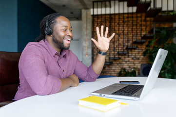 Happy African-American man with locks hair wearing wireless headset sitting at home office and...