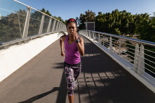 Fit african american woman running on foot bridge exercising in city
