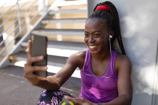 Smiling fit african american woman taking selfie with smartphone during exercise in city