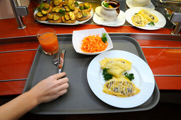 Hand put fork and knife on the tray with chebureks, salad and glass of juice placed on the canteen counter