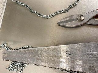 Large iron sharp metal scissors, metal cutters and a saw with chains lie on an iron table....