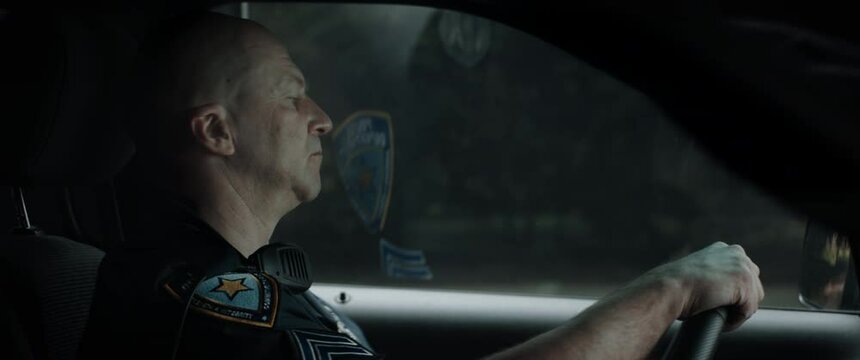 CU Caucasian American police officer patrolling streets of neighborhood in patrol vehicle. Shot with 2x anamorphic lens