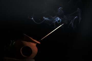 Burning incense on a white smoke censer on a black background is used as a background image of...