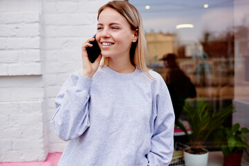 Happy female tourist in grey pullover enjoying positive international conversation during vacations, carefree hipster girl using roaming internet connection for friendly calling via mobile application