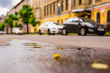 Sunny day after rain in the city, parked in the street car. Close up view from the level of the puddle on the pavement