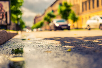 Sunny day after rain in the city, the headlights of the approaching car. Close up view from a puddle level near a curb