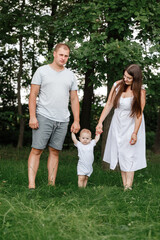 Happy young family, mom, dad and baby son spending time together outdoors in summer green garden